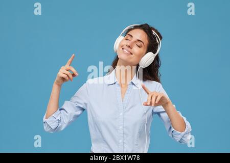 Portrait d'une jeune femme souriante dans un casque à l'écoute de musique et en appréciant sur fond bleu Banque D'Images