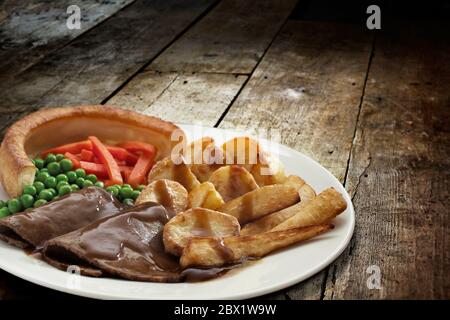 Dîner traditionnel avec rôti de bœuf, Yorkshire pudding et légumes servis dans une assiette sur une table en bois Banque D'Images