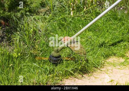 l'ouvrier tond l'herbe et les mauvaises herbes avec une tondeuse à gazon dans le pays Banque D'Images