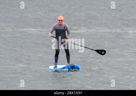 West Bay, Dorset, Royaume-Uni. 4 juin 2020. Météo Royaume-Uni. Une paddle-Boarder sur la mer à la station balnéaire de West Bay à Dorset, lors d'un après-midi de températures fraîches et de ciel couvert. Crédit photo : Graham Hunt/Alay Live News Banque D'Images