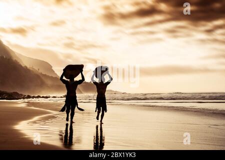 Des amis heureux qui couruent et tiennent des planches de surf sur la plage au coucher du soleil - le père et le fils de surfers faisant de l'exercice d'échauffement Banque D'Images