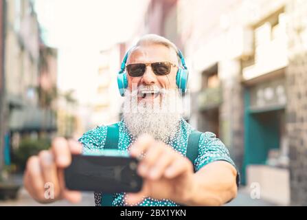 Homme senior barbu prenant selfie avec un téléphone mobile tout en écoutant la liste de lecture préférée avec un casque - branché hipster mâle s'amuser avec un smartphone Banque D'Images