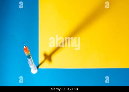 Seringue pour vaccin ou insuline, avec son ombre, sur fond bleu et jaune. Mise au point ponctuelle ou sélective. Concepts de santé, vaccination, coronarivu Banque D'Images