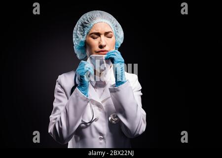 Photo de la femme fatiguée pleure exténuée doc retirer le masque de protection après la dernière opération en retard respiration air frais porter des gants laboratoire manteau blanc chirurgical Banque D'Images