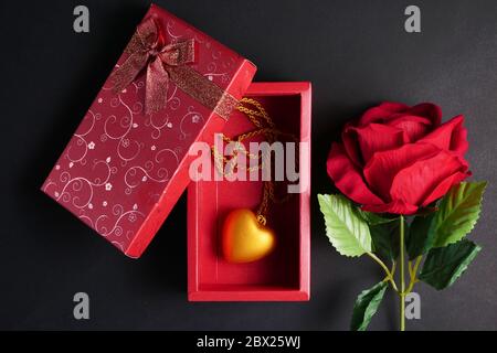 Collier à coeur doré rose rouge dans une boîte cadeau rouge sur fond noir. Concept de Saint-Valentin. Banque D'Images