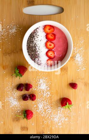 Bol à smoothie rose magenta aux baies, fait de bananes congelées, de framboises, de fraises et de lait de coco. Recouvert de flocons de noix de coco, de graines de chia et de fraises Banque D'Images