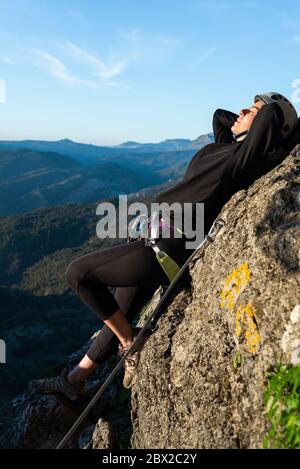 Concept : aventure. Femme grimpante avec casque et harnais. Couché sur un rocher prenant un bain de soleil. Faire via ferrata dans les montagnes. Banque D'Images