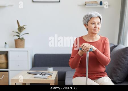 Femme âgée assise sur un canapé et regardant loin elle se reposant et pensant à quelque chose dans le salon à la maison Banque D'Images
