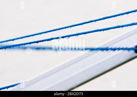 Les lignes de vêtements bleues d'un vêtement tournent avec de nombreux gouttes de pluie à la corde devant un fond clair, après la pluie. Une façon rétro de faire le linge Banque D'Images