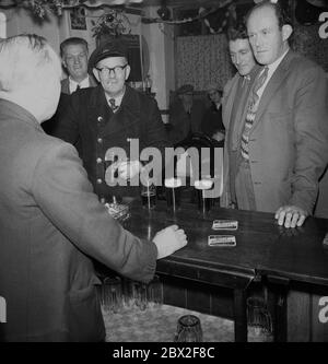 Années 1960, historiques, des hommes boivent des pintes de bière au bar d'un pub parlant au propriétaire, avec un monsieur tenant un tankard et fumant une cigarette, Angleterre, Royaume-Uni. Banque D'Images