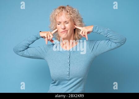 femme portant des vêtements bleus bouchant ses oreilles voulant arrêter le bruit fort. Banque D'Images