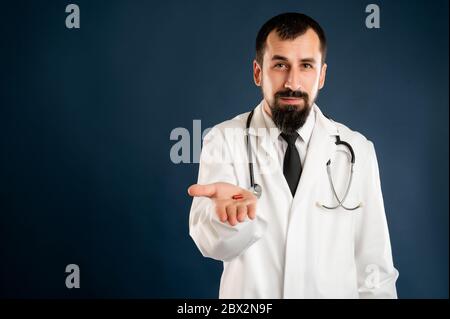 Portrait d'un médecin masculin avec stéthoscope en uniforme médical montrant des médicaments rouges posant sur un fond bleu isolé. Banque D'Images