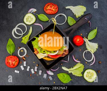 Savoureux hamburger de bœuf grillé dans un pain court croustillant avec laitue et légumes frais sur fond noir de pierre. Banque D'Images