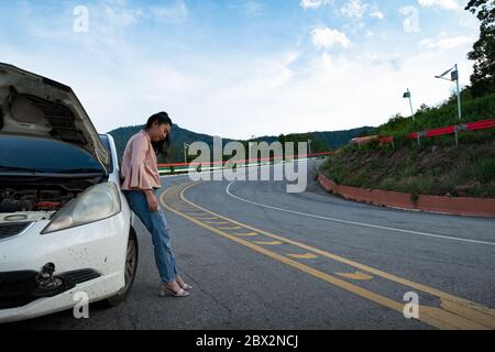 Une jeune belle dame se tenant près de la voiture pour appeler à l'aide sur la route publique dans la zone forestière à la montagne et le ciel fond Banque D'Images