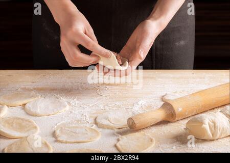 Vue avant des mains de femme faisant des boulettes de viande avec une goupille en bois. Le processus de fabrication de boulettes maison, étape 10. Viande hachée sur la pâte, le Banque D'Images