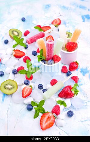 Des papoles de fruits entiers et sains avec des fraises Berries Kiwi sur fond clair, avec un décor de glace, de menthe. Une délicieuse glace aux fruits dans le mug. Espace de copie. Banque D'Images