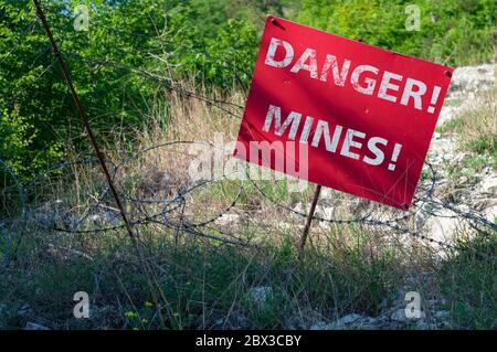 Panneau rouge DANGER MINES devant un champ de mines clôturé avec un fil barbelé Banque D'Images