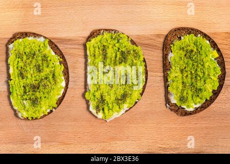 Trois sandwichs avocat sur un panneau en bois. Pain brun, purée d'avocat et épices. Recette végétarienne. Banque D'Images