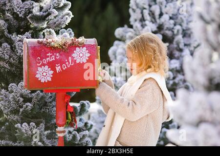 Jolie blonde maurie fille avec lettre près de la boîte aux lettres du Père Noël Banque D'Images