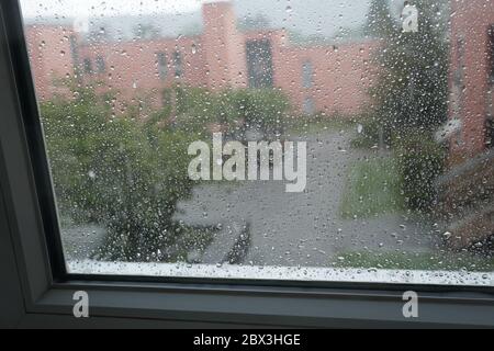 pluie sur le panneau de la fenêtre déformant la vue de la cour en silhouettes et contours . Banque D'Images