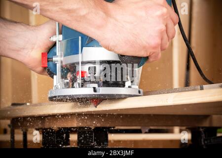 gros plan de menuisier avec machine à router à la main en bois au travail. gros plan de l'acheminement d'un biseau dans la planche de pin bois de construction concept d'outil fournit Banque D'Images