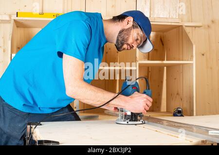 menuisier avec machine à router à la main en bois au travail. gros plan de l'acheminement d'une fente dans la planche de pin bois de construction outil concept de mobilier fabrication d Banque D'Images
