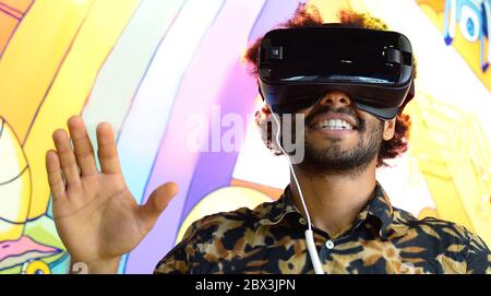 Le gars gai à la peau sombre s'est plongé dans le monde virtuel, portant des lunettes de réalité virtuelle. Portrait d'un afro-américain positif avec afro Banque D'Images