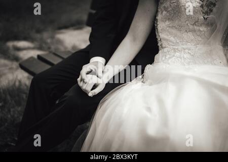 Photo noir et blanc du couple de mariage assis sur le banc. Gros plan sur le genou des bras. Sans tête. Concept de mariage. Banque D'Images