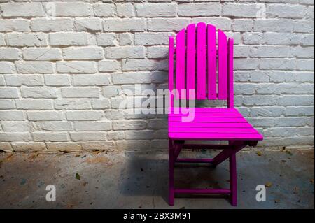 Chaise pliante en bois rose contre un mur en brique blanche Banque D'Images