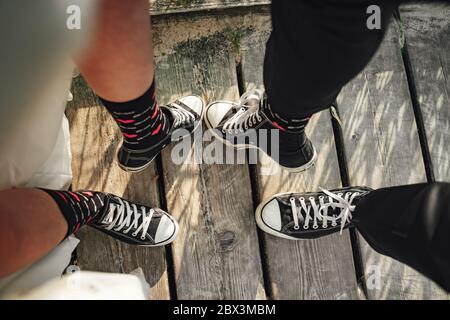 Jambes pour mariée et marié avec baskets noires et blanches. Couple de mariage sur une promenade en bois près de la mer portant des chaussures décontractées. Banque D'Images