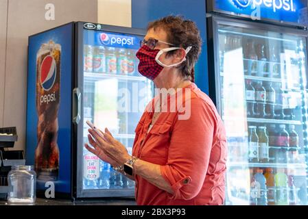 Une femme mature tenant un téléphone portable porte un masque facial en tissu en attendant dans un restaurant de San Ramon, Californie, le 25 avril 2020. () Banque D'Images