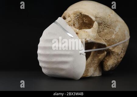Crâne isolé sur fond noir et noir, portant un simple masque en papier pour la protection contre les vapeurs d'odeurs ou les virus. Corona Covid-19 Banque D'Images