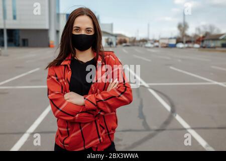 Une fille dans un masque médical est assise sur un banc dans la rue. Portrait d'une fille dans un masque sur la rue. Concept de pandémie de coronavirus. Masque dans la rue. Banque D'Images