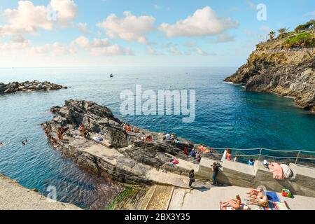 Les touristes se baigner dans la mer et le soleil près de la de la côte rocheuse de Manarola, Italie, une partie de la région des Cinque Terre. Banque D'Images