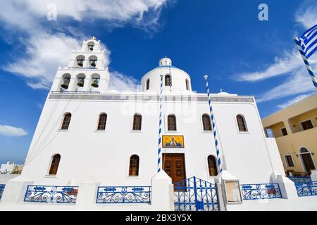 L'église de Panagia Platsani avec un drapeau grec volant dans le village perché d'Oia, sur l'île de Santorin, Grèce. Banque D'Images