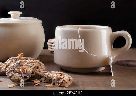 Une tasse de thé avec des biscuits aux pépites de chocolat au granola sur le côté et une casserole de sucre sur fond noir Banque D'Images