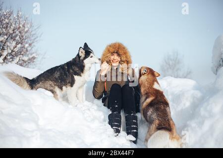 Bonne jeune fille embrassant des huskies rouges et noires en hiver Banque D'Images