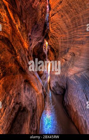 Une longue exposition de lumière douce et chaude disséminée dans la piscine dans le tunnel Slot Canyon coloré dans le Grand Staircase-Escalante National Monument dans l'Utah. Banque D'Images