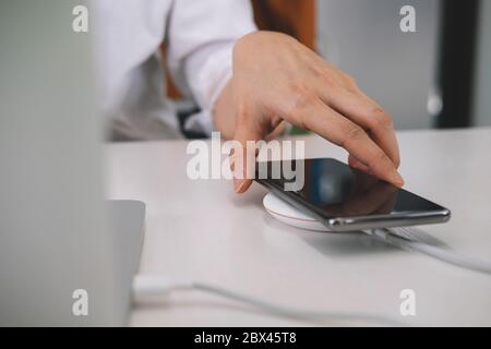 Femme d'affaires travaillant sur le lieu de travail et se chargeant de téléphone mobile avec un appareil sans fil Banque D'Images