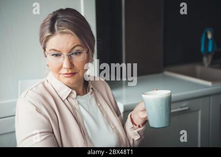Femme caucasienne concentrée avec des lunettes buvant une tasse de thé et travaillant à distance de la maison Banque D'Images