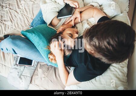 Jolie fille caucasienne avec des cheveux bruns couchés sur son petit ami dans le lit couvert d'une courtepointe et tenant un livre Banque D'Images