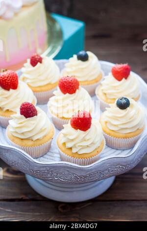 Petits gâteaux à la vanille avec glaçage au fromage à la crème et baies fraîches, myrtille et fraise. Arrière-plan rustique. Banque D'Images