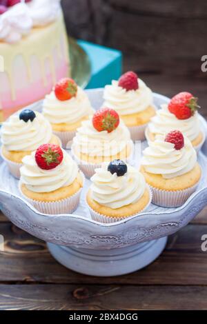 Petits gâteaux à la vanille avec glaçage au fromage à la crème et baies fraîches, myrtille et fraise. Arrière-plan rustique. Banque D'Images