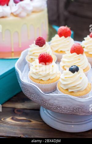 Petits gâteaux à la vanille avec glaçage au fromage à la crème et baies fraîches, myrtille et fraise. Arrière-plan rustique. Banque D'Images