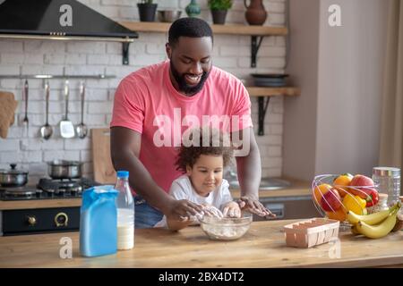 Mignon petit poil et son père jouant avec de la farine dans la cuisine Banque D'Images