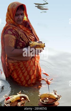 La femme hindoue indienne offre de la nourriture à dieu soleil sur Les rives de la rivière pendant les rituels de Chhath Puja Banque D'Images