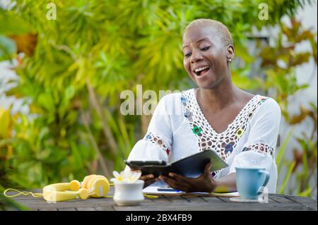 Jeune femme afro-américaine hippster noire heureuse et attrayante travaillant avec une tablette numérique en plein air dans un café décontracté et gai dans le nomad numérique suces Banque D'Images