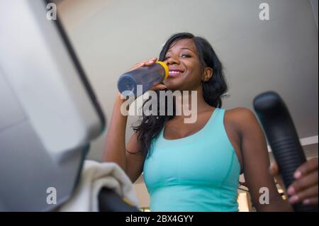 Intérieur gym portrait de jeune attrayant et heureux noir afro américaine entraînement machine elliptique entraînement à l'entraînement au club de fitness sourire gai drin Banque D'Images
