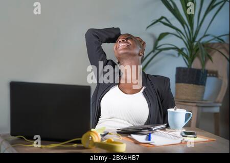 jeune femme afro-américaine noire heureuse et réussie penchée sur une chaise de bureau excitée et joyeuse travaillant au bureau d'ordinateur portable sur un lieu de travail moderne dans Banque D'Images
