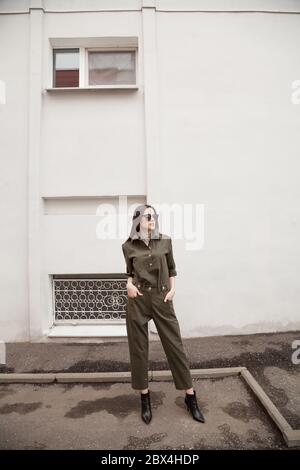 élégante et belle jeune femme dans un costume vert tendance avec des lunettes de soleil posant dans la rue dans l'environnement urbain. Style professionnel tendance Banque D'Images